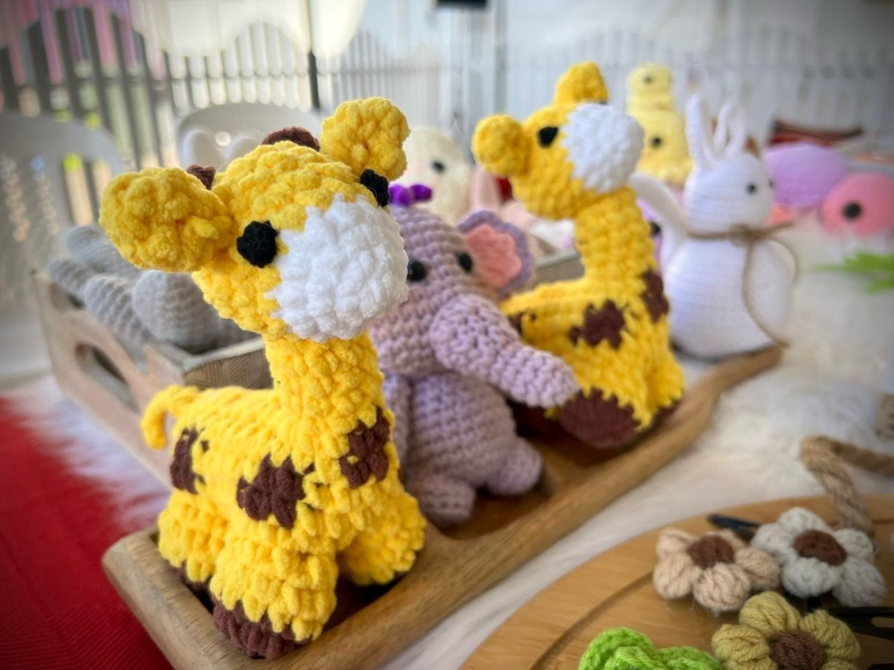A pair of hand-crocheted giraffe amigurumi and a small lavender elephant, warmly lit indoors.