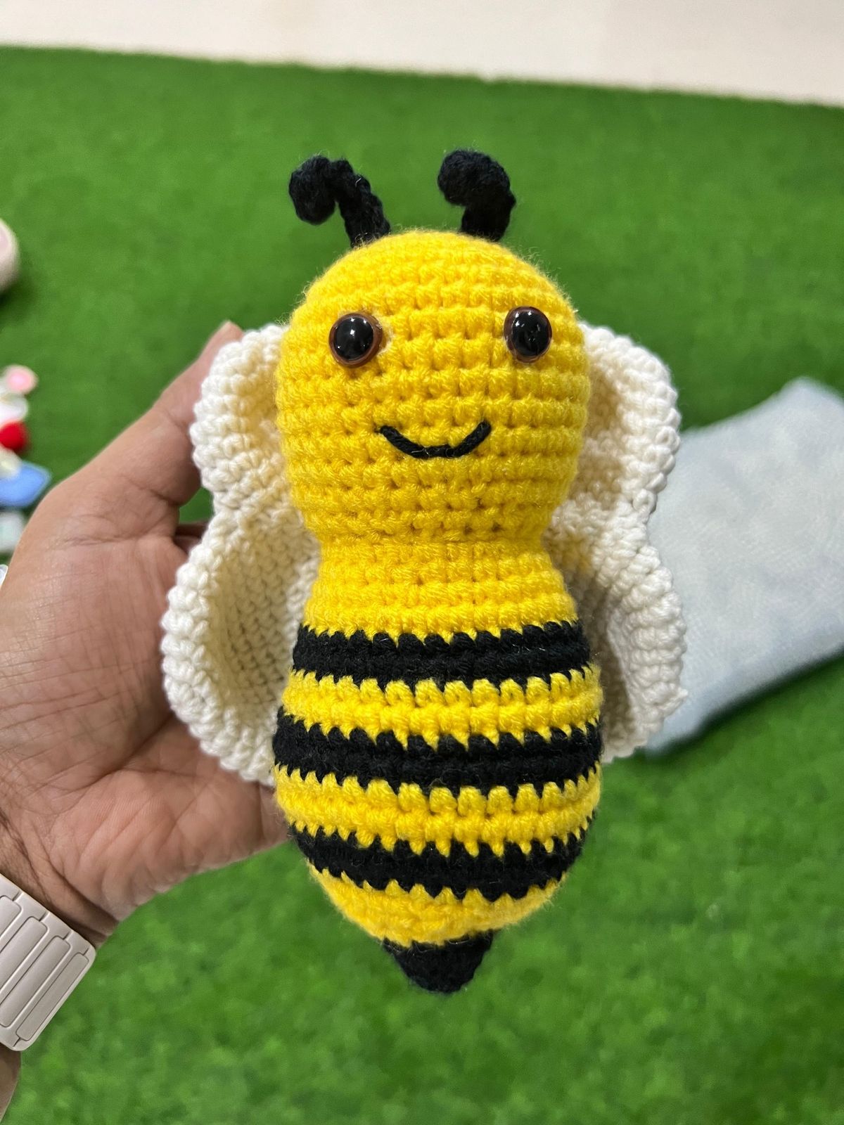 A hand holding a small finished crochet bumblebee amigurumi against a green grass background.
