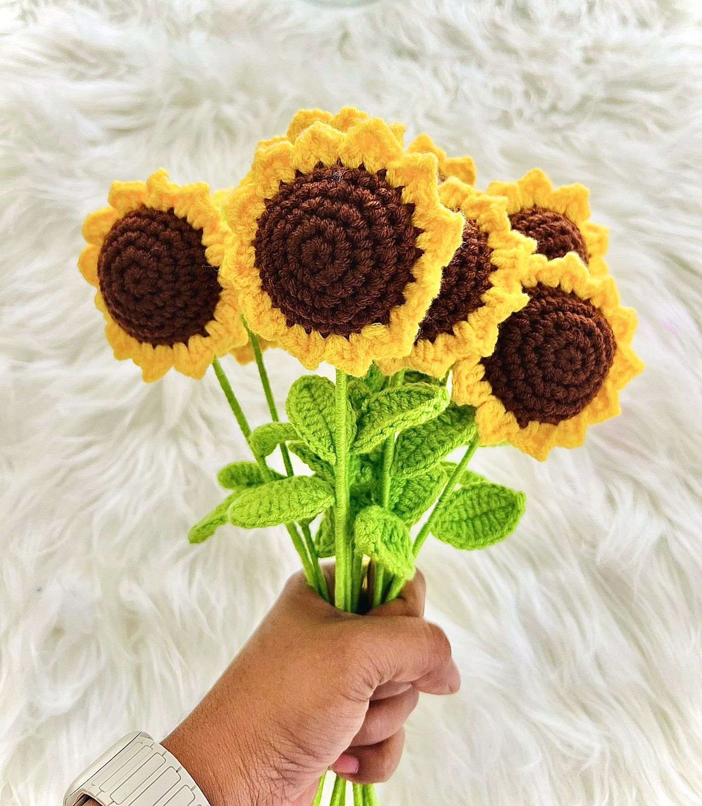 A handful of hand-crocheted sunflowers with brown centers and yellow petals, held up against a soft white fur background.